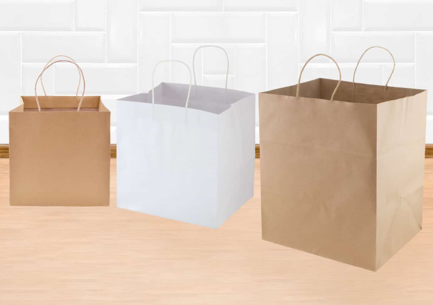 Three paper bags with handles sitting on a wood floor in front of a tiled wall.